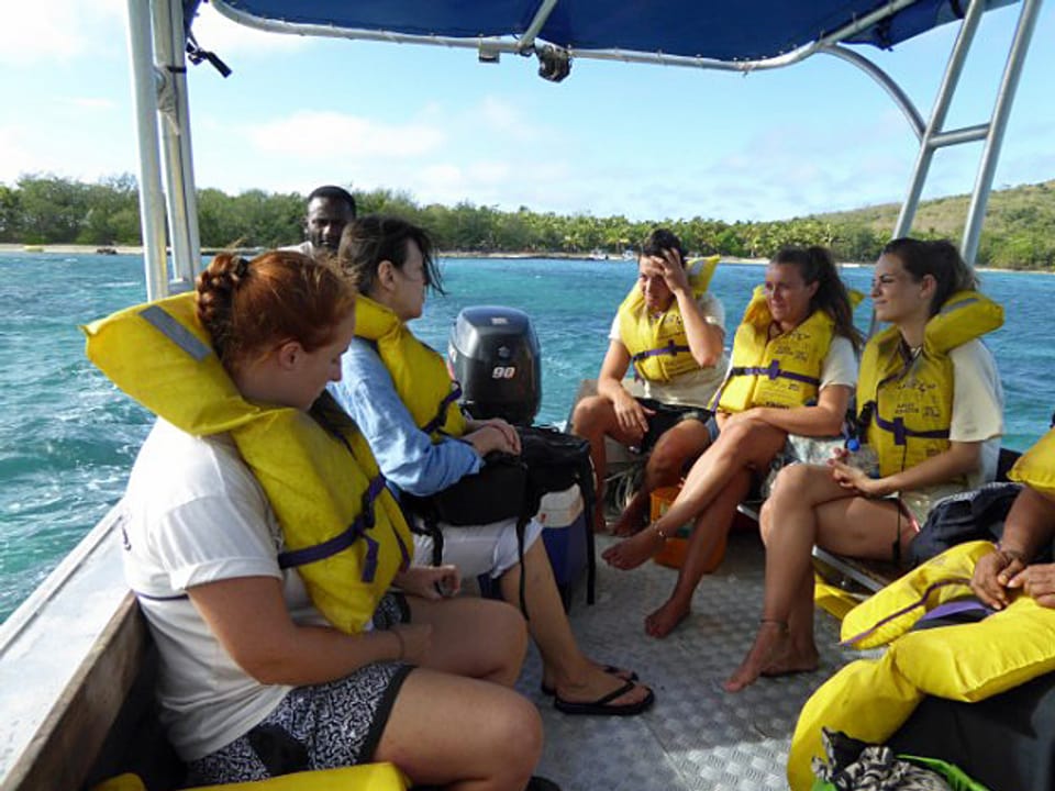Auf einem Boot sind mehrere junge Touristinnen und Touristen mit montierten Schwimmwesten zu sehen.