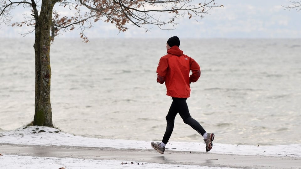 Ein Mann joggt bei einem See. Es hat Schnee. 