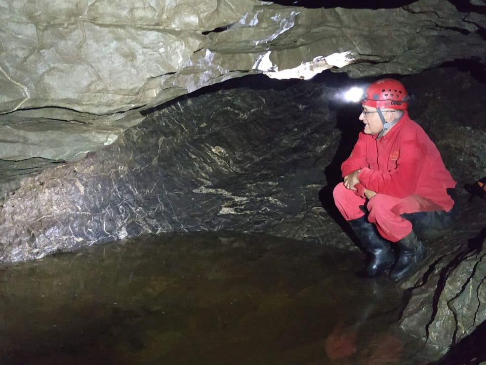 Mann in einer Höhle mit Helm und Stirnlampe. Schaut in Wasser.