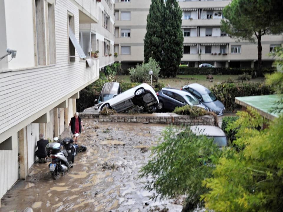 Zusammengeschogbene Autos vor überfluteten Garagen im Erdgeschoss eines Wohnhauses.