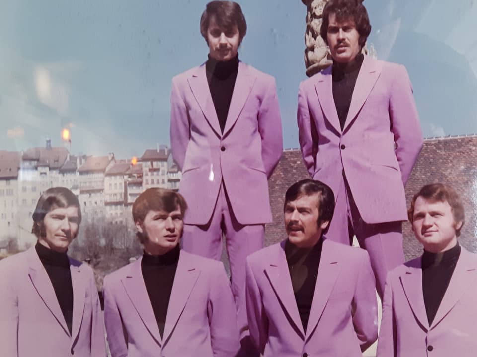 Sechs Musiker in pinkfarbenen Kostümen. 