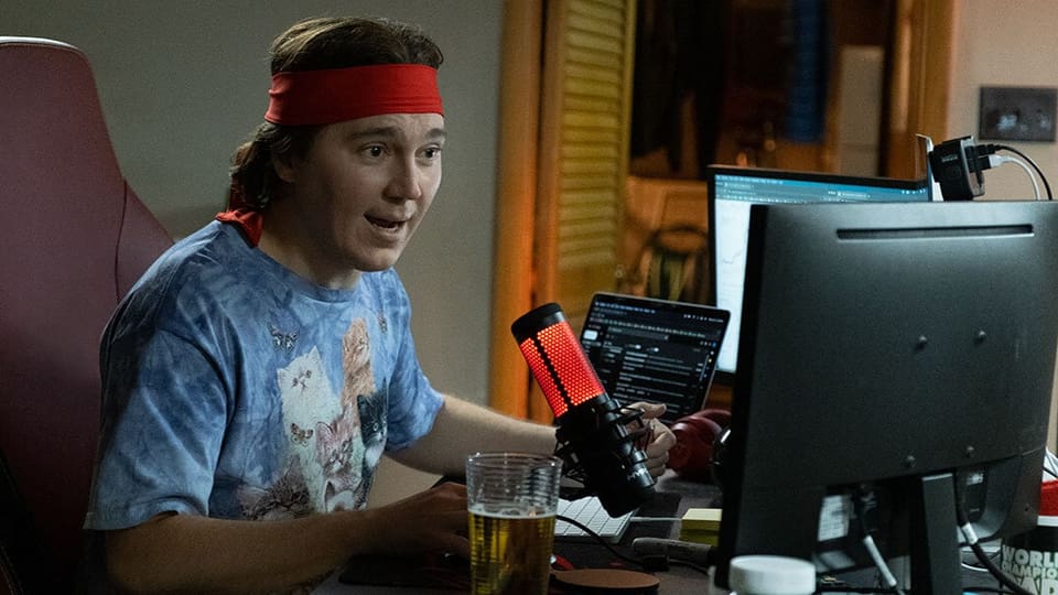 a young man sits in front of his computer with a microphone.