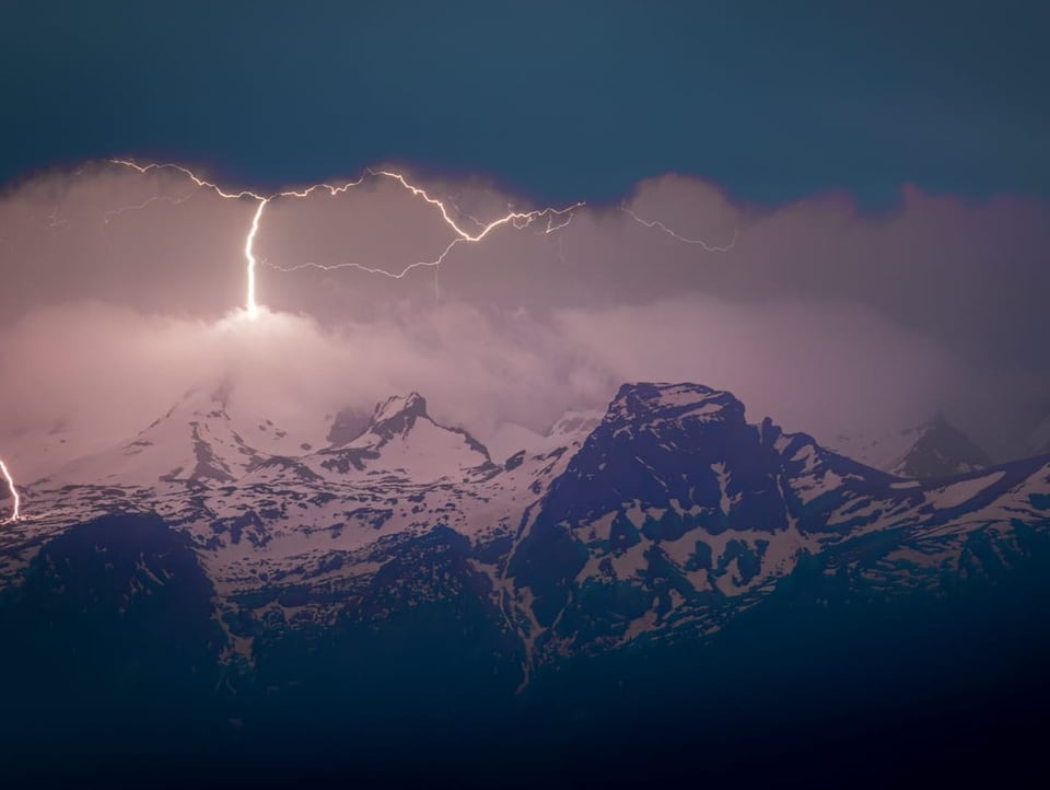 Nachhimmel wird von Blitz erhellt, der in Alpengipfel einschlägt, der noch verschneit ist. 