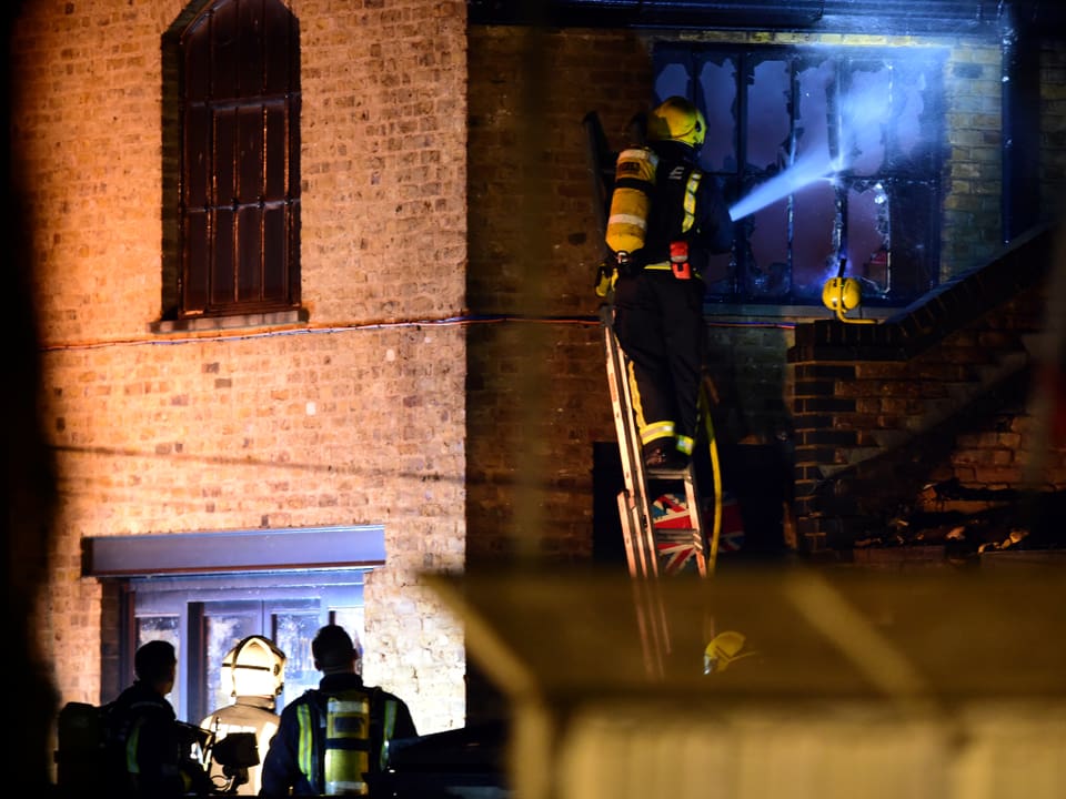Feuerwehrmann auf Leiter an einem Backsteingebäude mit Fenstern