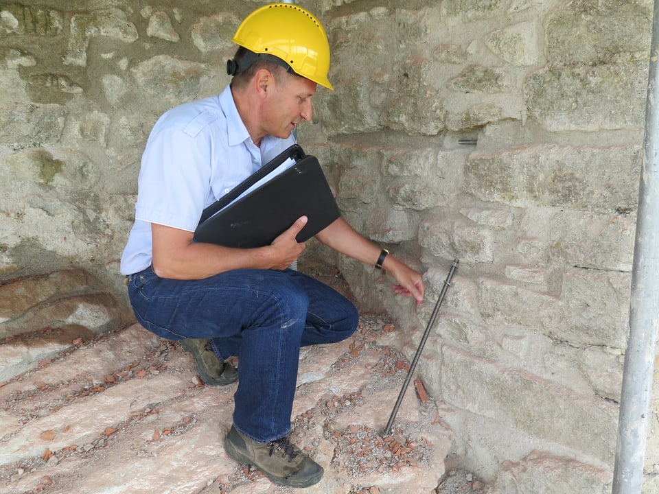 Projektleiter Rainer Kaufmann zeigt die Gewindestangen, welche zur horizontalen Stabilisierung in die Mauer eingebaut werden (klein zu sehen in der Mauer).