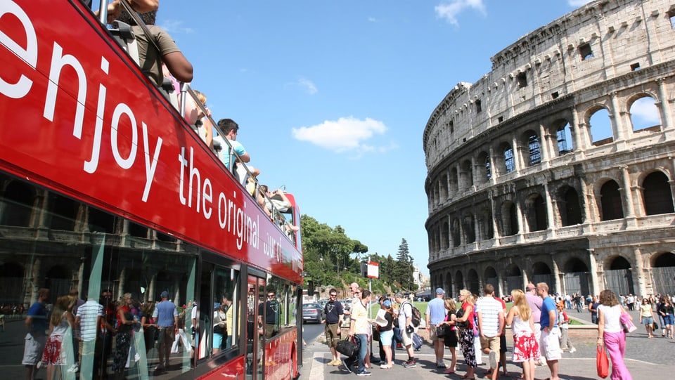Touristen fahren mit einem Doppeldeckerbus am Kolosseum in Rom vorbei