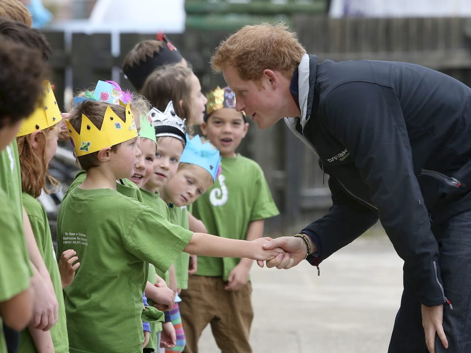 Schulkinder mit gebastelten Kronen empfangen Prinz Harry an ihrer Schule.