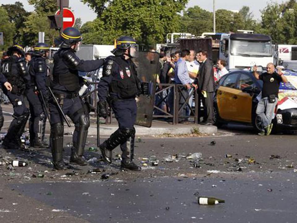 Polizisten in Kampfmontur schreiten zu Autokollone.