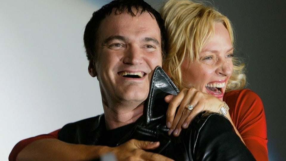 Quentin Tarantino wird von hinten von Uma Thurman umarmt. Beide strahlen dabei um die Wette.