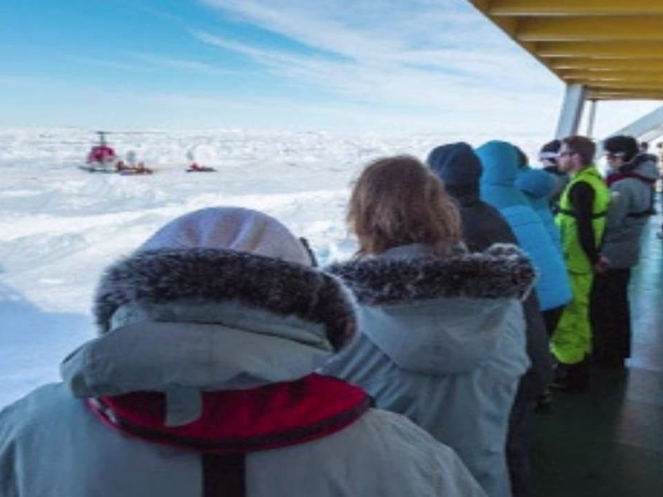 Passagiere schauen auf den auf dem Eis gelandeten Helikopter.