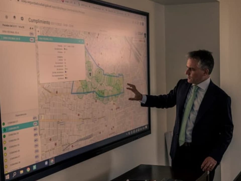 Minister D'Alessandro zeigt auf einen Stadtplan auf einem grossen Bildschirm.