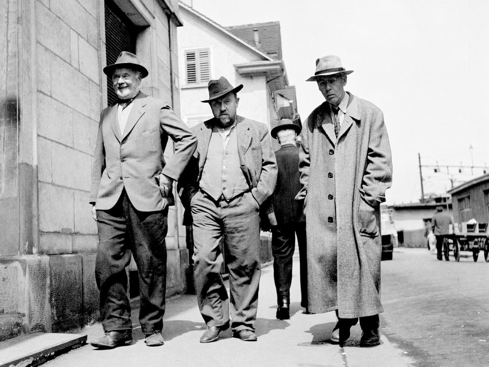 Drei Männer gehen eine Strasse entlang.