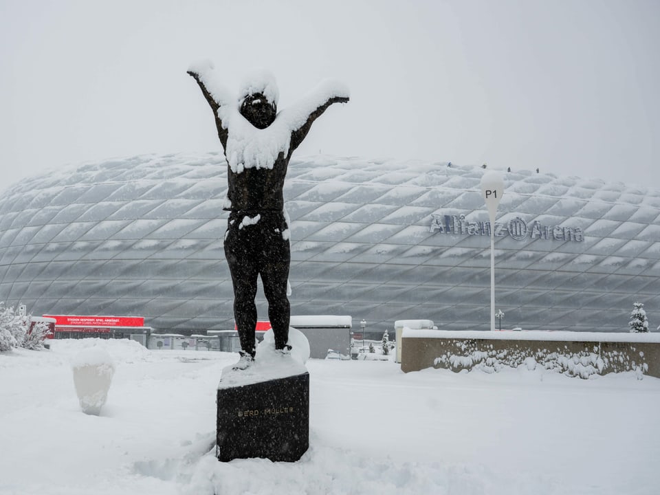 Eingeschneite Statue von Gerd Müller, im Hintergrund die Allianz Arena