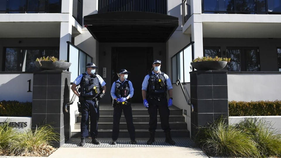 Drei Beamte vor einem Gebäude mit Masken