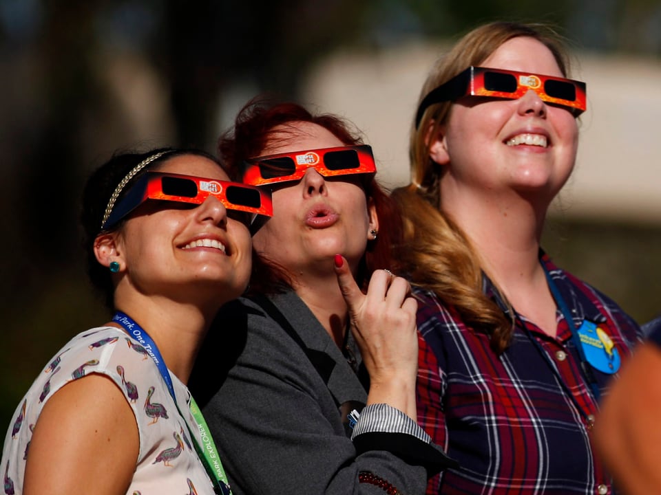 Drei Frauen beobachten die Sonnenfinsternis mit einer Schutzbrille.