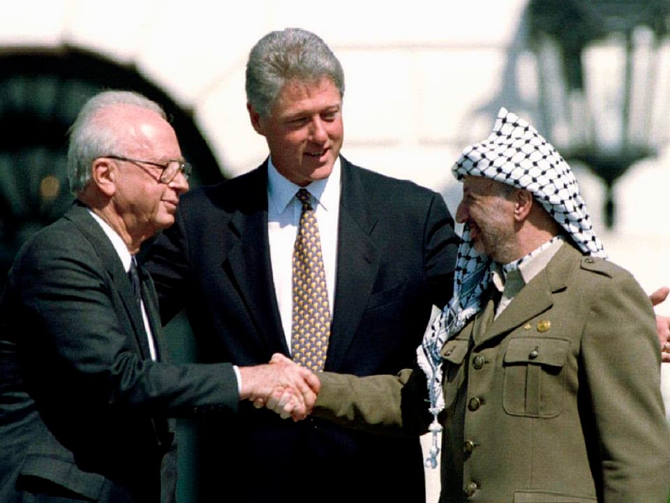 Bill Clinton steht zwischen Jitzhak Rabin und Jassir Arafat, die sich die Hände geben.