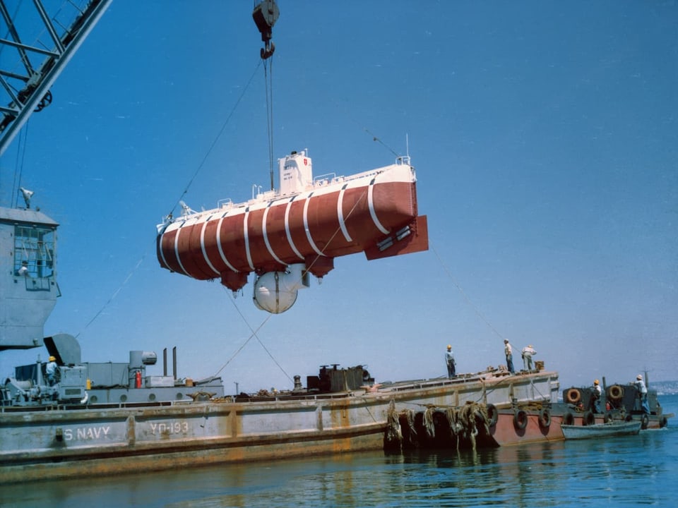 Ein Kran auf einem Schiff lässt ein rotes U-Boot zu Wasser