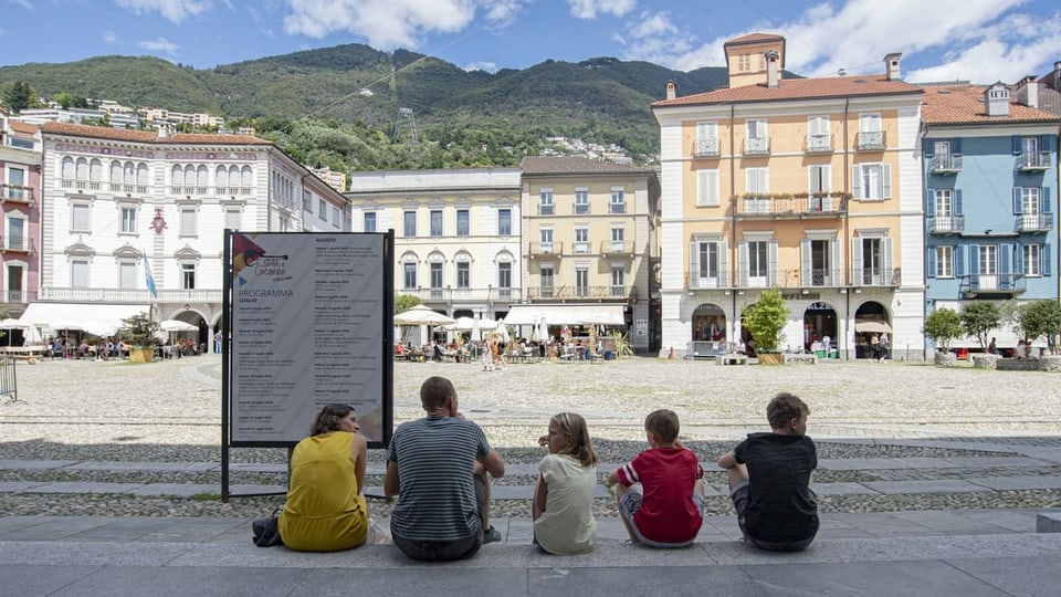 Familie mit drei Kindern sitzt am Rand der leeren Piazza Grande