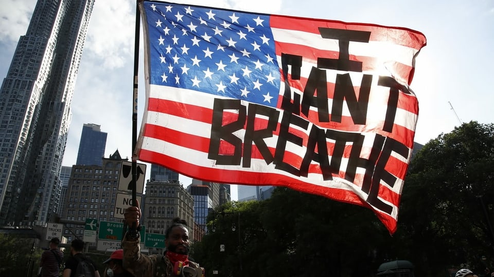 ein Mann hält eine US-Flagge mit den Wörtern "I can't breathe" auf
