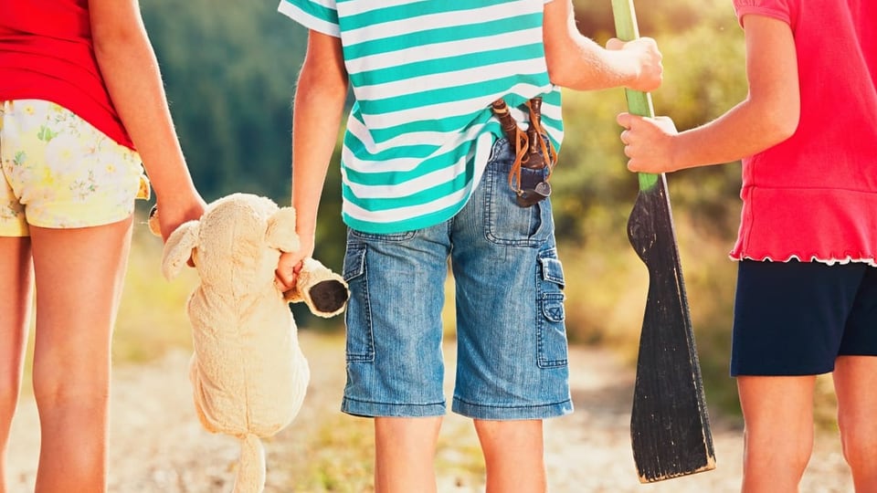 Drei Kinder mit einem Holzgewehr und einer Steinschleider. 