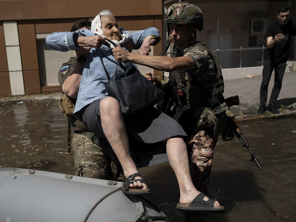 Zwei Soldaten hieven eine alte Frau aus einem Schlauchboot. 