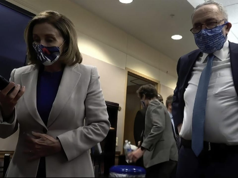 Nany Pelosi und Chuck Schumer mit Masken in einem Gang, sie mit Handy