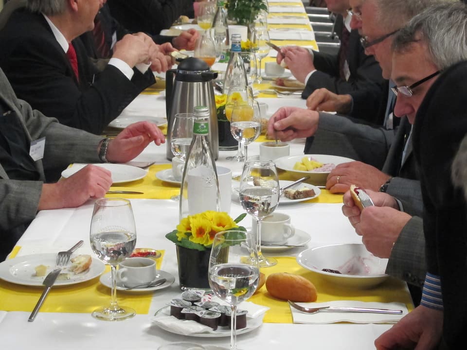 Tischreihe mit vielen Tellern und Händen, die am essen und trinken sind.