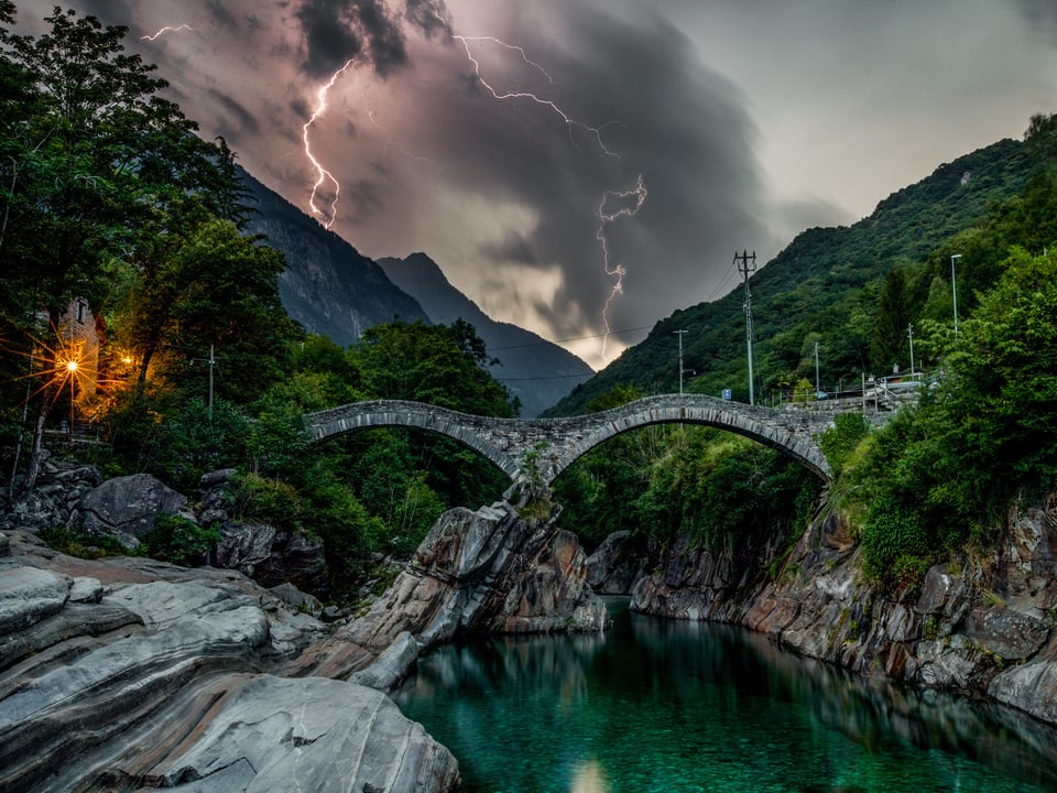 Hinter der bekannten Doppelbrücke von Lavertezzo entladen sich Blitze.