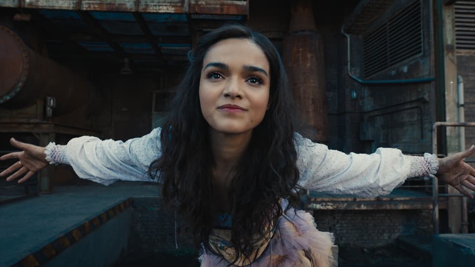A woman stretches her arms and looks directly into the camera.