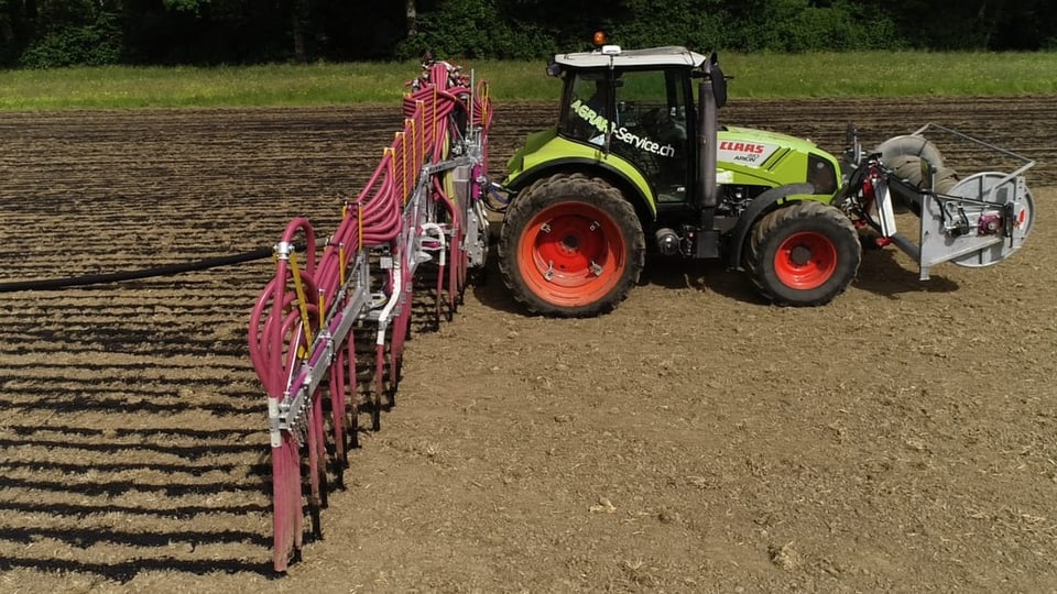 Ein Traktor fährt im Bild von links nach rechts und versetzt das Feld mit Gülle.