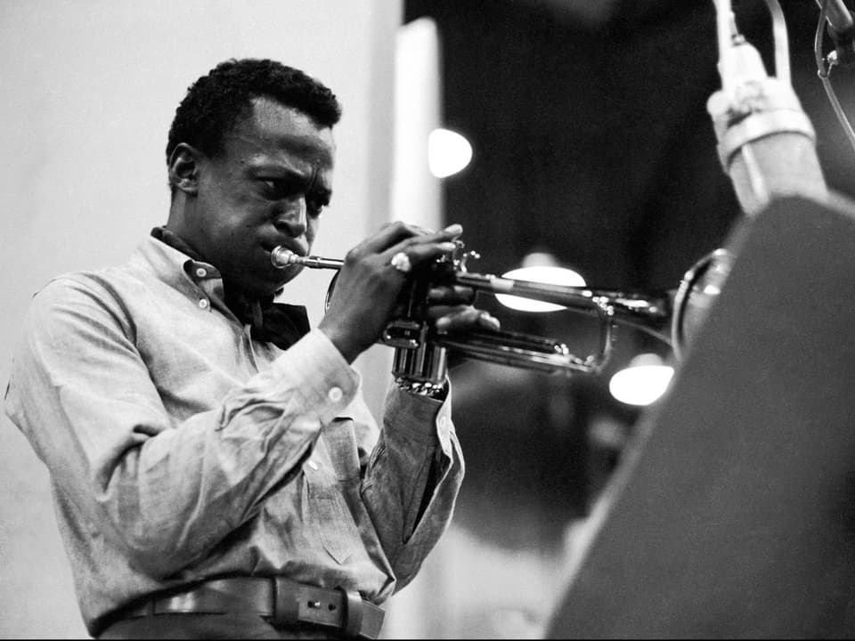Miles Davis im Studio Trompete spielend vor grossem Mikrofon.