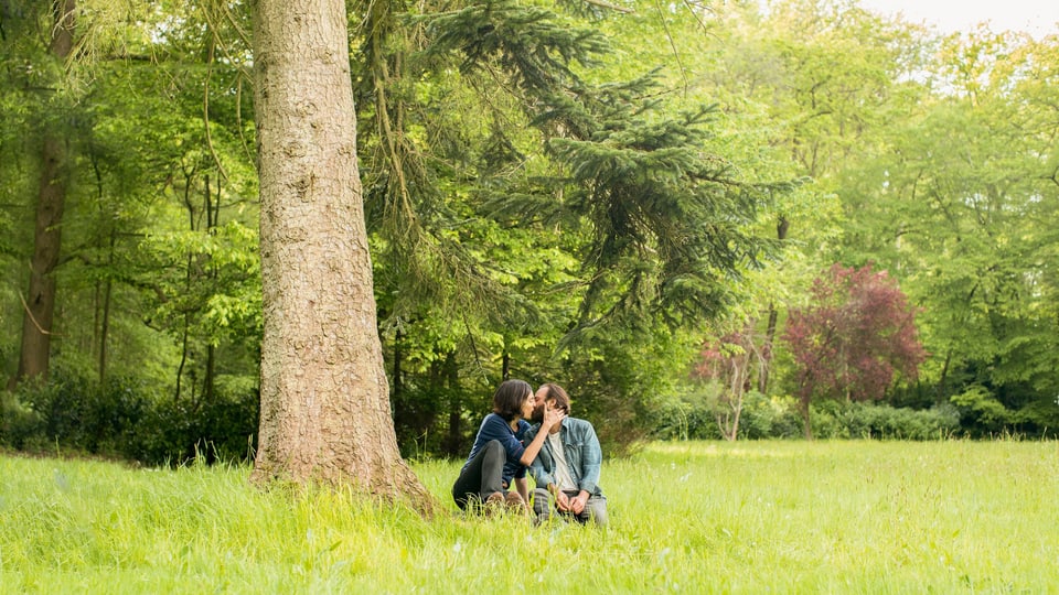 Ein Mann und eine Frau küssen sich unter einem Baum.