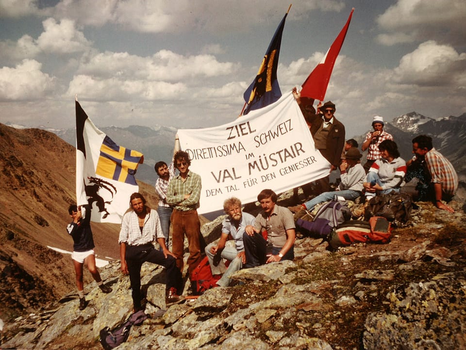 Gruppenfoto mit Alpinisten und Sympathisanten, die Kantonsfahnen schwingen und ein Transparent mit «Ziel Val Müstair» zeigen.
