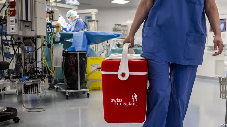 Eine Person trägt einen Kühlkoffer in einem Operationssaal.