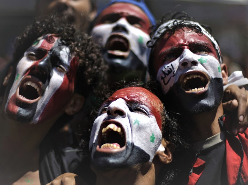 Demonstranten mit jemenitischen und syrischen Flaggen auf ihren Gesichtern skandieren Slogans während einer Demonstration. Die arabische Schrift auf dem Gesicht des Mannes lautet «Raus hier».