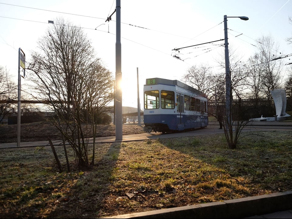 Ein blaues-weisses Tram verlässt in der Morgensonne die Endstation.