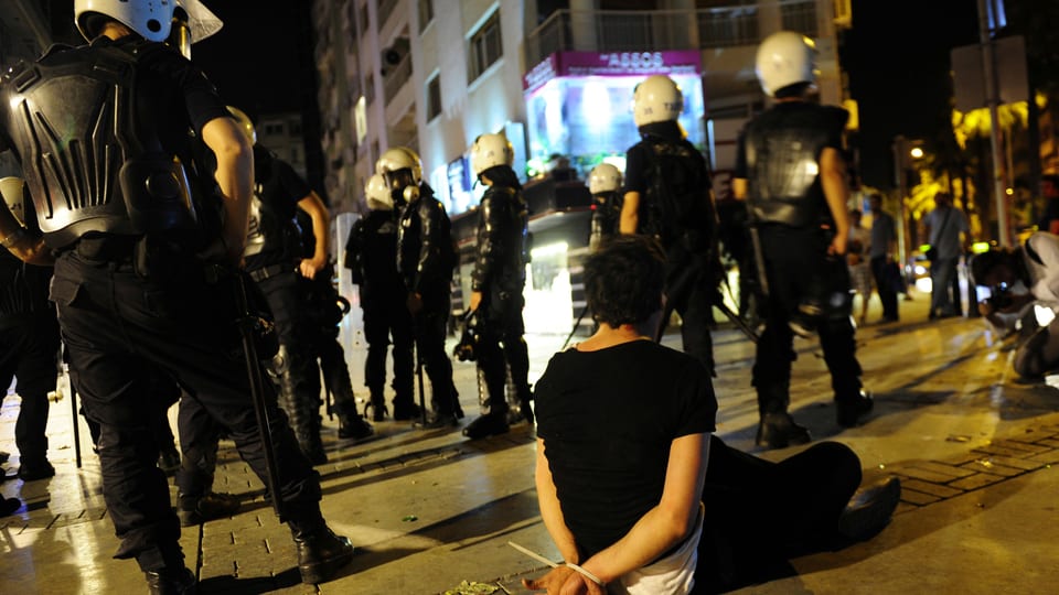 Ein Demonstrant sitzt mit zusammengebundenen Armen hinter vielen Polizisten in Izmir. 