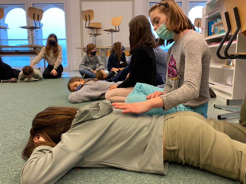 Schüler aus der Montessori Schule liegen in einem Kreis und hören eine Geschichte. 