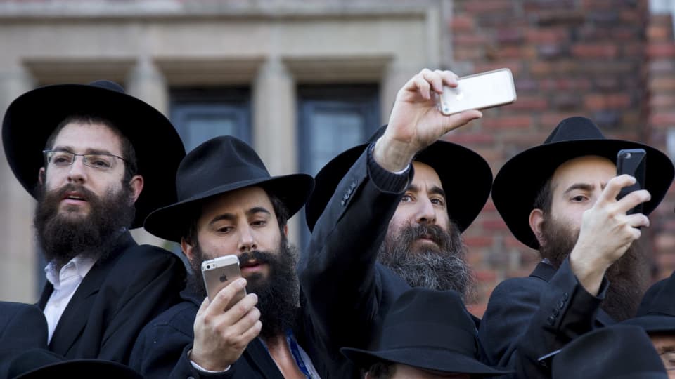 Chassidische Juden mit Bärten, schwarzen Hüten und Smartphones