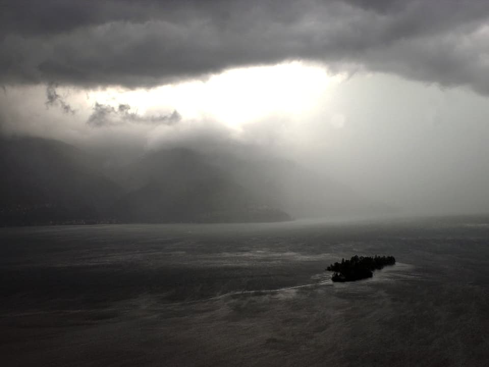 Im Lago Maggiore sind die Brisagoinseln zu sehen. Bedrohlich schwarzer Himmel und dichte Regenschleppen schränken die Sichtweite stark ein.