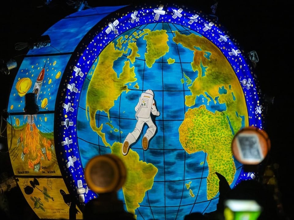 Eine grosse Laterne, die eine Weltkugel zeigt, im Vordergrund ist ein Astronaut.
