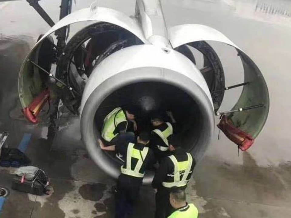 Vier Männer schauen ins Innere eines Flugzeug-Triebwerk. 