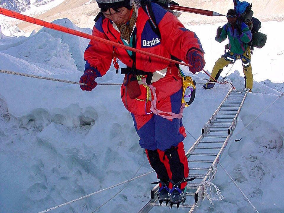 Mount-Everest-Besteiger läuft angeseilt über eine Aluminiumleiter, die eine Gletscherspalte überwindet.
