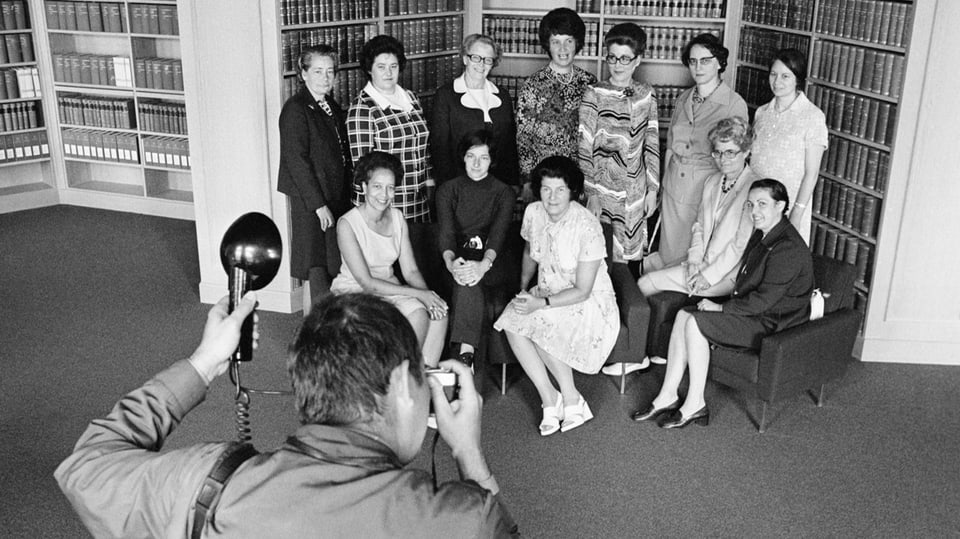 Schwarzweissfoto: Frauen posieren in der Gruppe, im Vordergrund ein Fotograf.