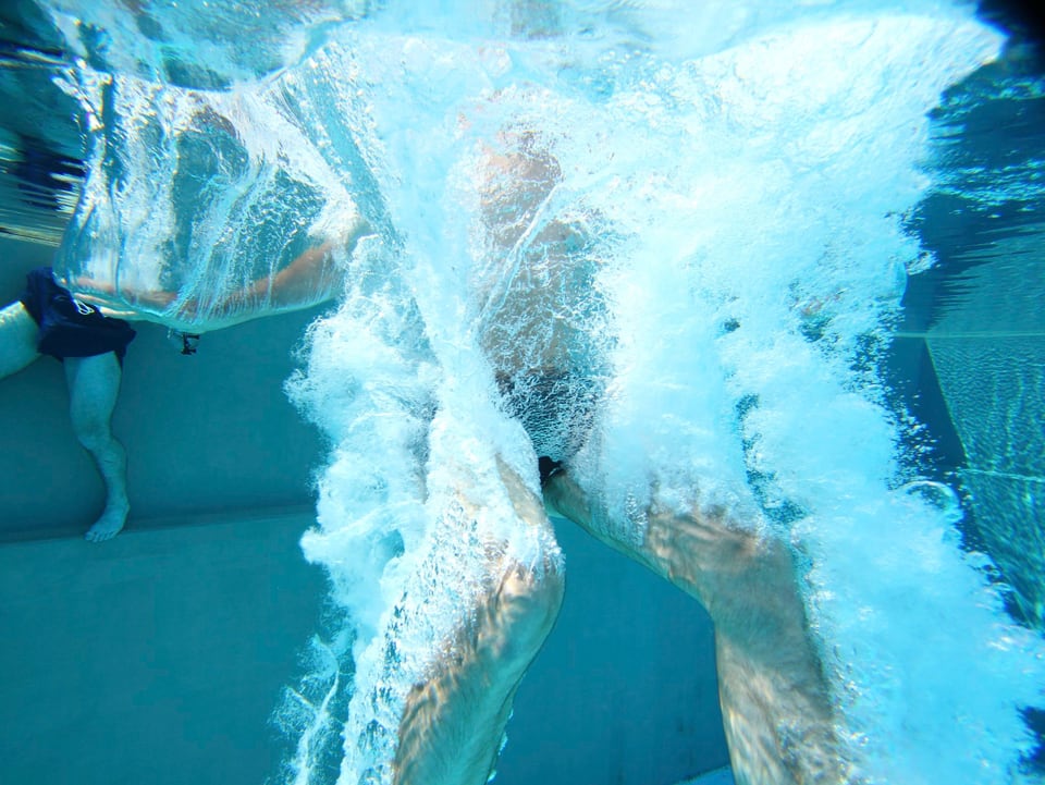 Unterwasserfoto eines beinvoran ins Wasser tauchenden Mannes.