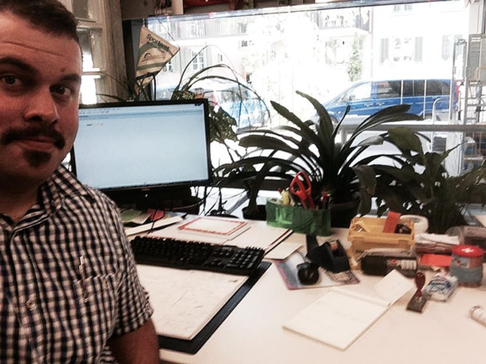 Mann mit modischem Schnauz an seinem Arbeitsplatz mit Computer und Pflanzen.