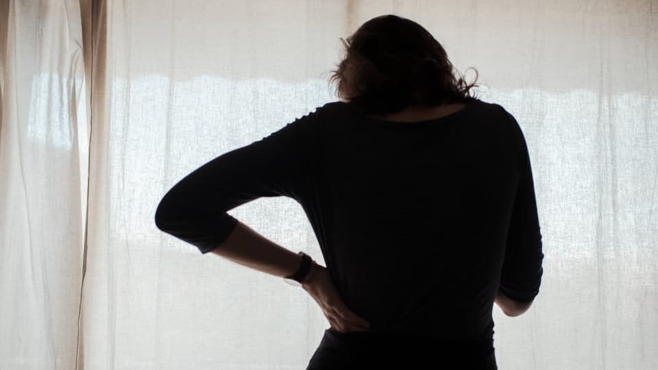 Silhouette des Rückens einer Frau, die vor einem Vorhang steht.