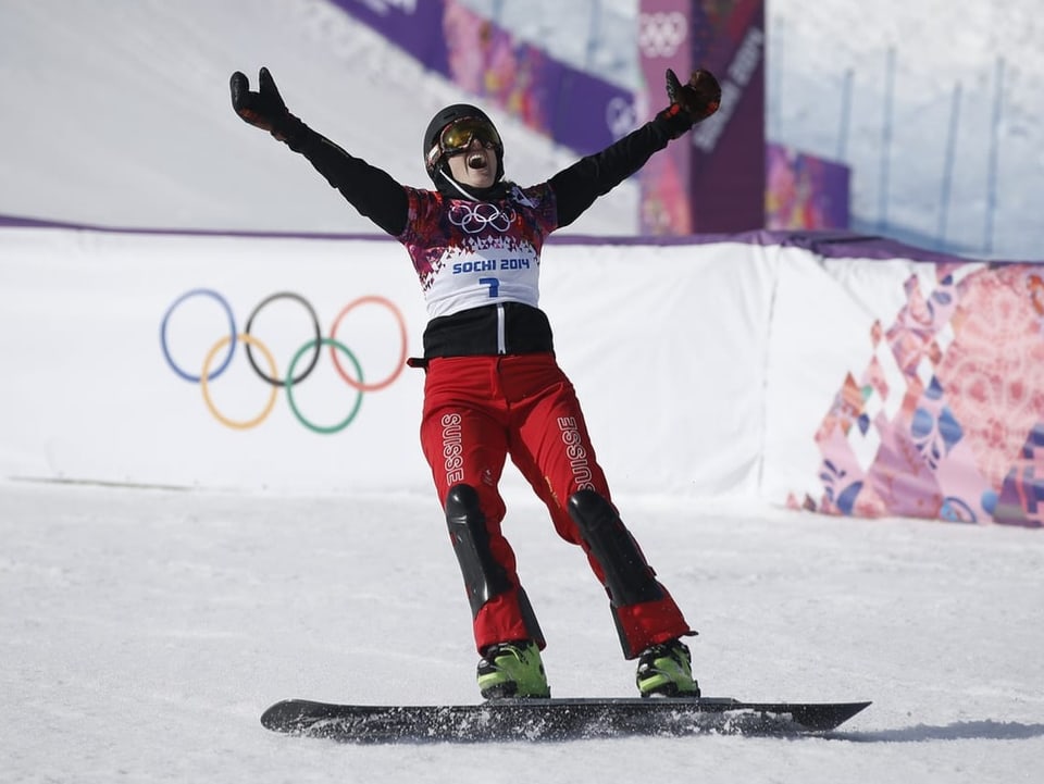 Patrizia Kummer mit Snowboard auf der Piste, hebt die Hände vor Jubel.