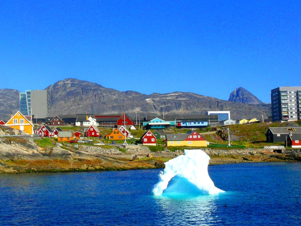 Eisberg vor Küste, farbige kleine Häuser, zwei graue Blocks.