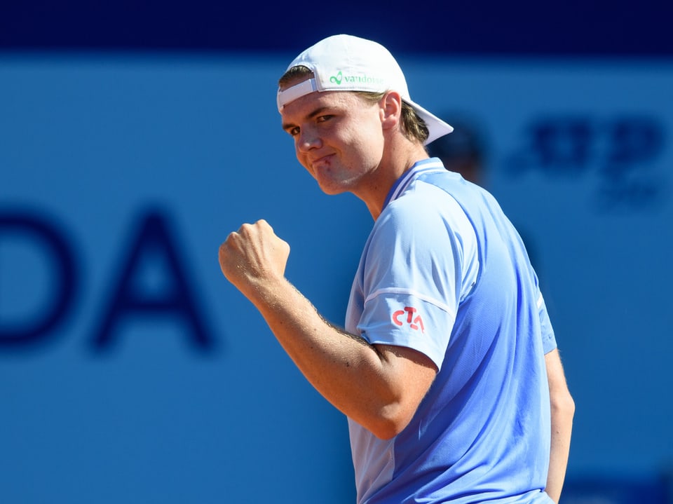 Tennis player in white cap showing fist in cheering gesture.